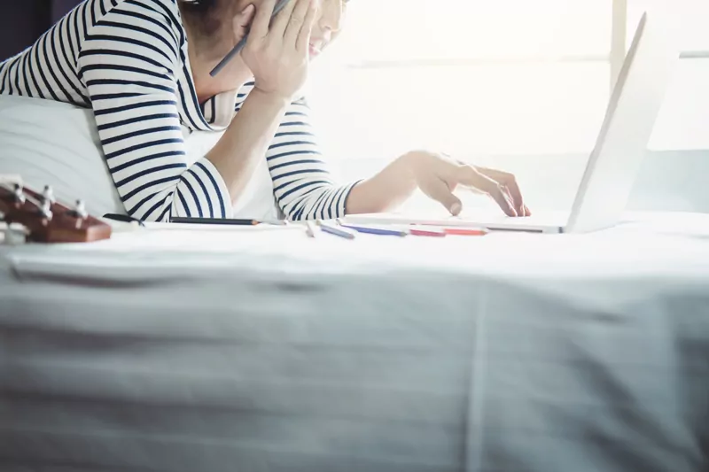 Eine Frau sitzt auf ihrem Bett und arbeitet an einem Laptop